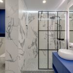 Elegant bathroom featuring marble walls, double sinks, and a glass-enclosed shower.